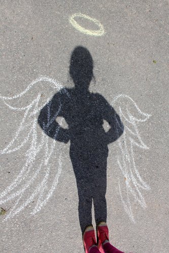 En ängel bildas av skuggan frånv ett barn tillsammans med vingar ritade med krita på asvalten.