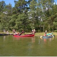 Strandbild där människor paddlar med kanoter.